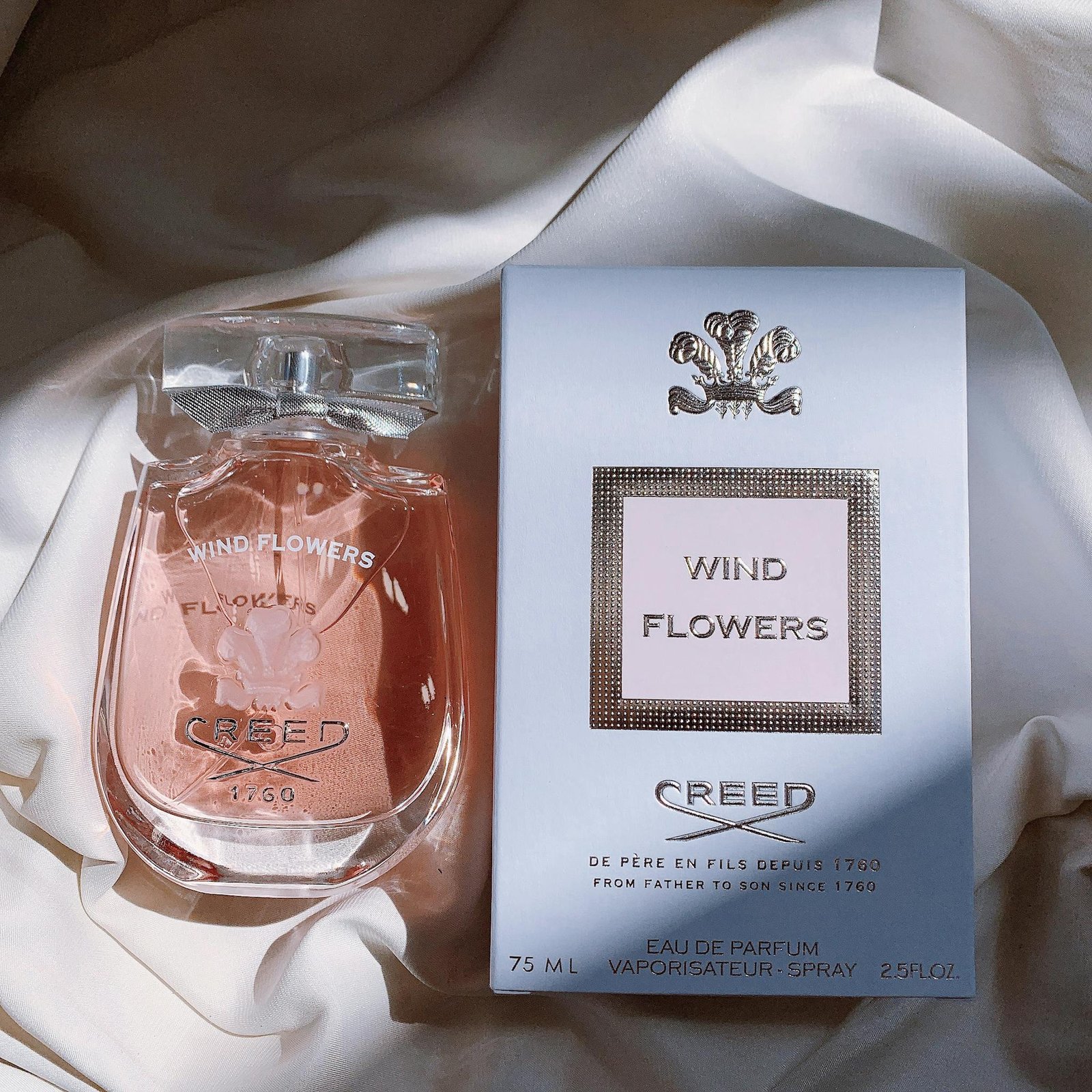 Sophisticated perfume bottle and box displayed on soft fabric with natural light.