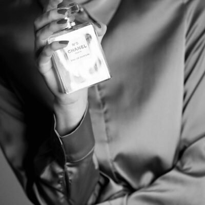 Stylish black and white photo of a woman holding a perfume bottle, exuding sophistication.