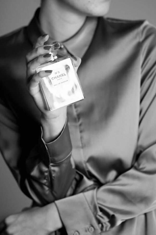 Stylish black and white photo of a woman holding a perfume bottle, exuding sophistication.